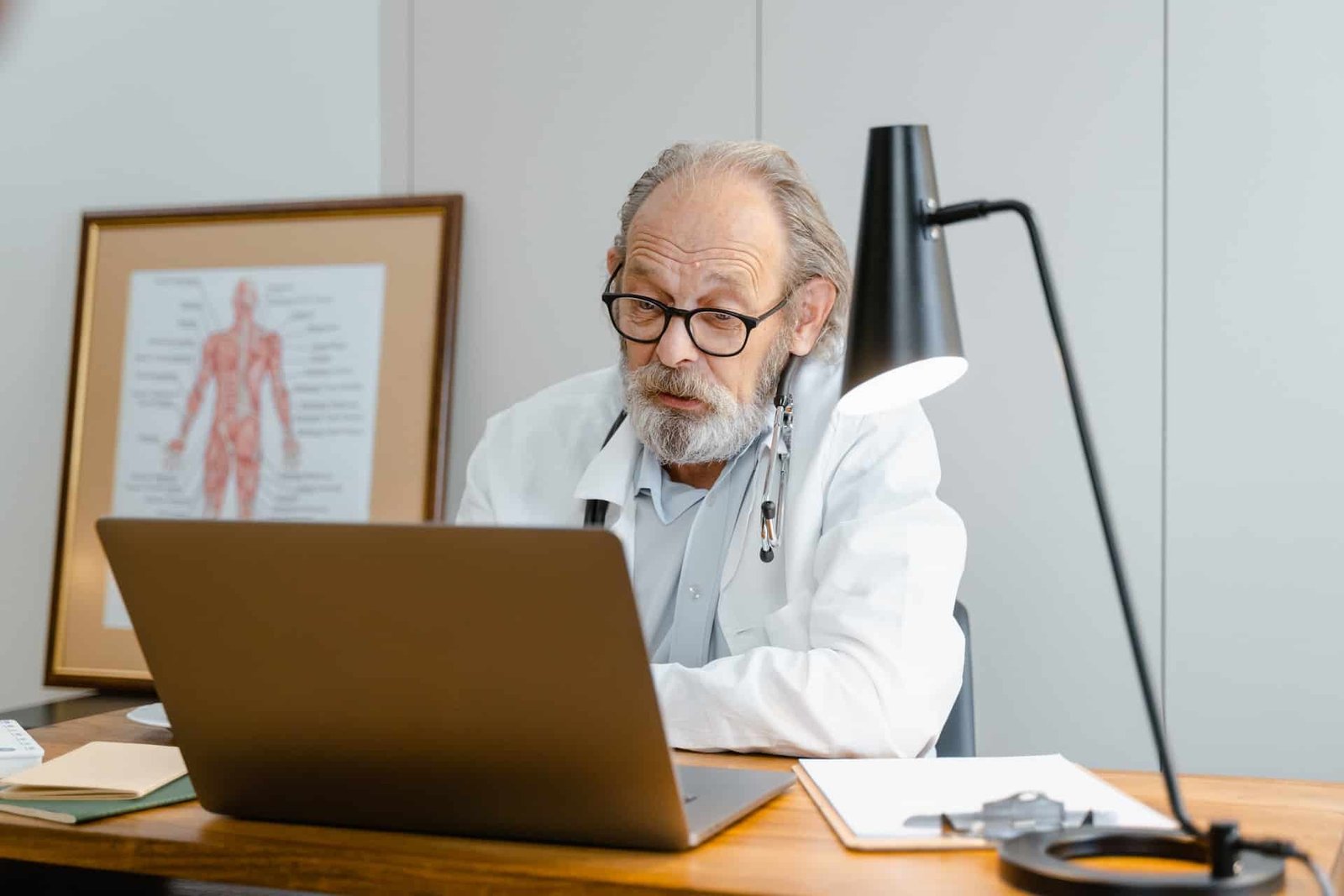 A doctor at a desk looking through patient messages on his laptop.