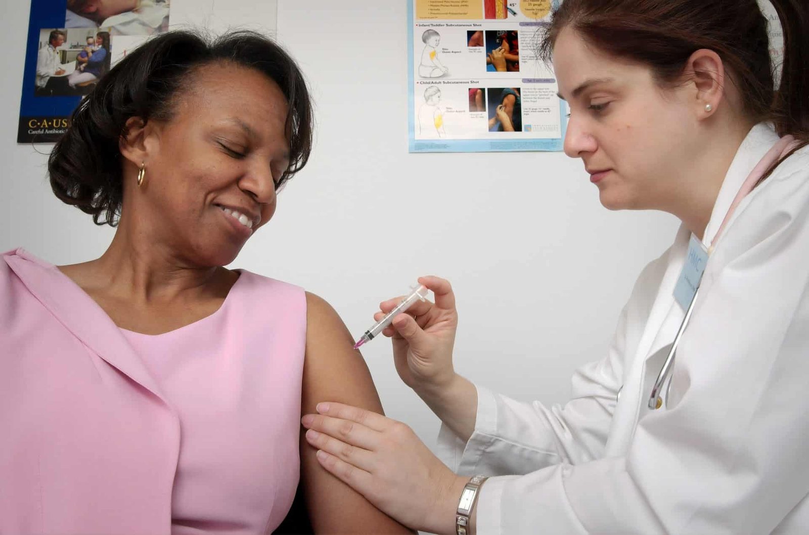 A doctor giving a smiling woman a shot in her upper arm. 