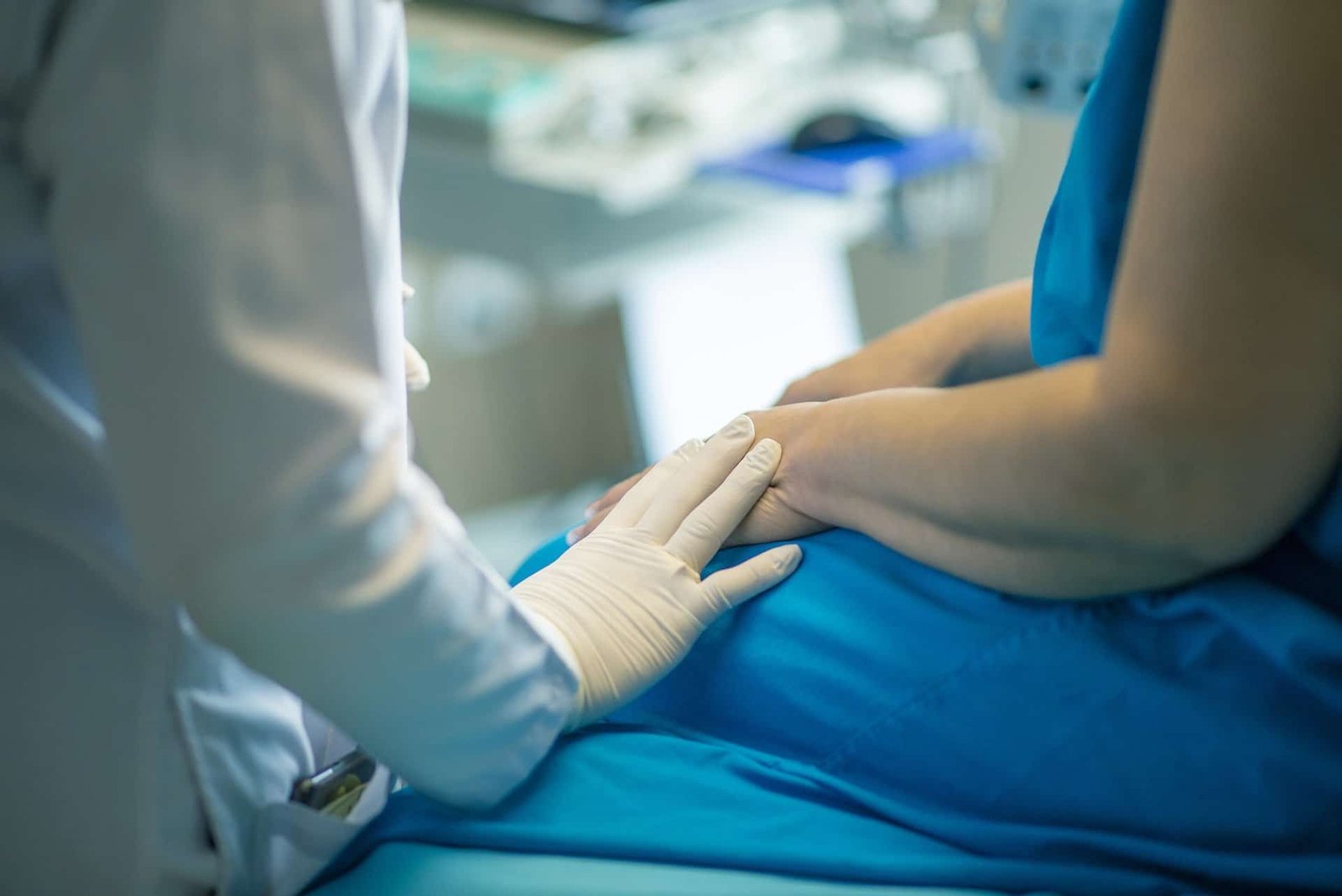 a doctor putting one hand on the arm of a patient in a blue hospital gown