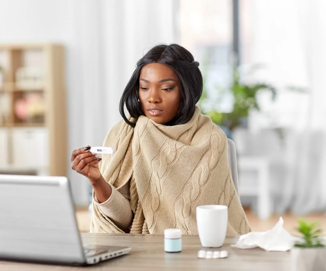A woman with a fever checking her symptoms online to see if she should go to the doctor.